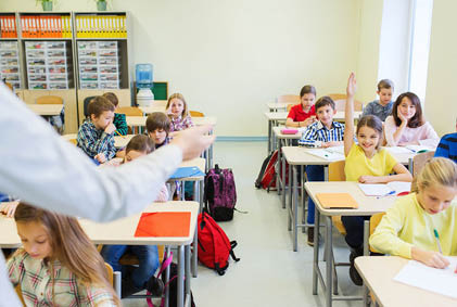 education, elementary school, learning and people concept - group of school kids with teacher sitting in classroom and raising hands