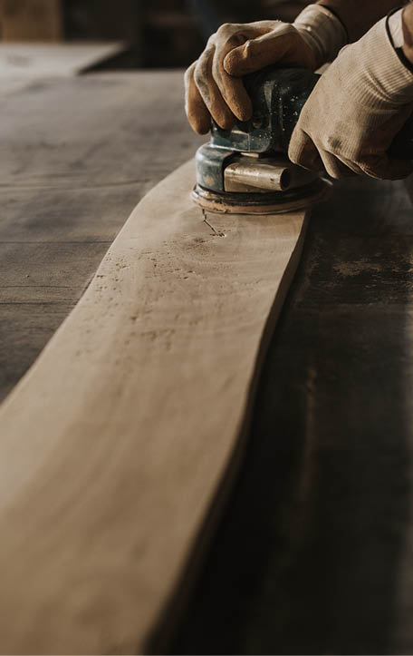 Unrecognizable manual worker using plane while working on a wood in a workshop.